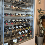 Vinoteca climatizada en Saraiba Restaurante con botellas de vinos gallegos y una planta decorativa, reflejando el ambiente acogedor para maridajes en Madrid
